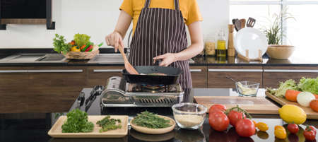 Chef in brown apron cooking steak. The kitchen counter full of various kinds of vegetables and seasonings.の写真素材