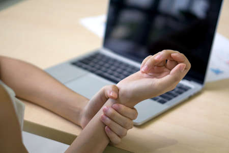 Young woman injured her wrist from using laptop computer for a long time. Closeupの写真素材
