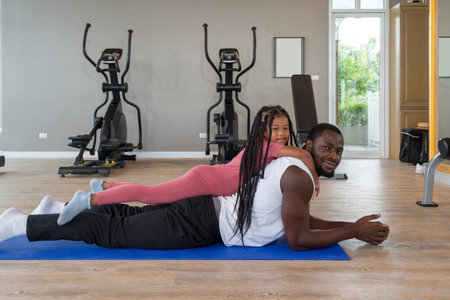 Young short curly black hair man relax on yoga mat while the  daughter are on his back. Happy family...