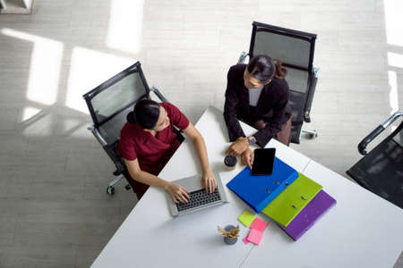 Two asian businesswoman meeting in modern office with laptop computer, tablet, document folder and coffee on table. People corporate business team concept. Top Viewの写真素材
