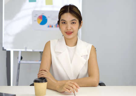 Asian businesswoman in white dress looking at camera, recording self-presentation video or sharing professional skills. Happy young smart people filming educational lecture.の写真素材