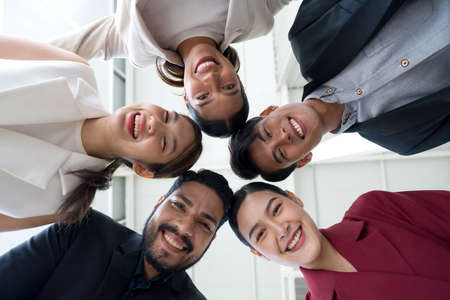 Portrait closeup bottom view happy faces of employees team standing in circle, looking at camera.の写真素材