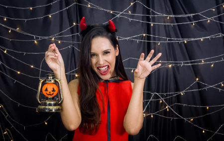 Happy Halloween! Caucasian woman holding a pumpkin lantern stand in front of black decoration wall at halloween party. Beautiful Glamour Fashion make up and costume.の写真素材