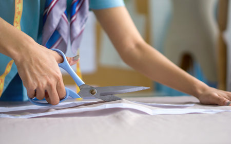 Closeup dressmaker hand use scissors to cut fine beige fabric.の写真素材