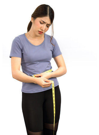 Young asian woman in exercise clothes use a tape measure to measure around the waist. Looked at the...