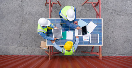 Group of shipment worker in hardhat and safety vest meeting on a table made of large solar cell...