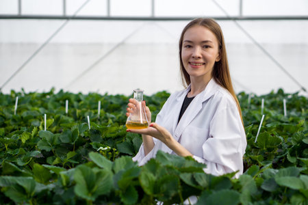 Caucasian female botanical scientist in white gown holding  Erlenmeyer flask with yellow chemical...