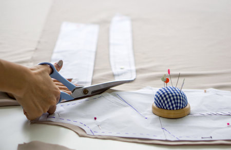 Closeup dressmaker hand use scissors to cut fine beige fabric and sketch paper pattern.の写真素材