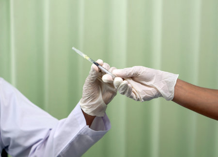 A nurse in medical gloves hands a syringe to a doctor in white gown. Closeup