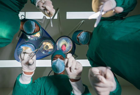 Emergency surgical care concept. Group of surgeons and nurse in surgical green gown uniform performing surgical operation in operating room. Bottom view.の写真素材