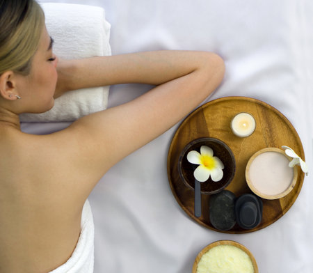 Herb, salt scrub, hot stone massages and scented candle on wooden trays. Aroma massage equipment on the massage table place next to young female customer. Top viewの写真素材
