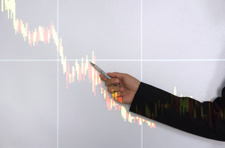 A professional man, donned in a fitted business suit, as he intently point towards an upward trending stocks chart highlighted on a digital screen.の写真素材