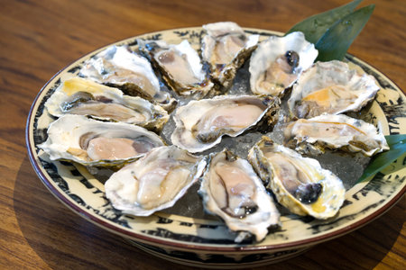 A bounty of fresh oysters resting on crushed ice within a rustic bowl. The bowl is positioned at the...