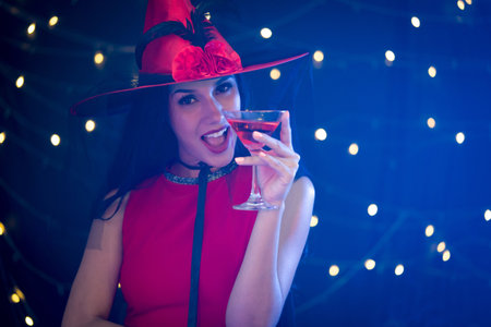 The enchanting essence of Halloween with an image of a woman donning a witch hat, gracefully holding a glass of wine.の写真素材