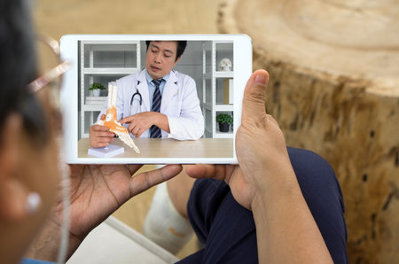 Back view of woman Telehealth consultation on the tablet screen with a male doctor with lab coat and stethoscope.の写真素材