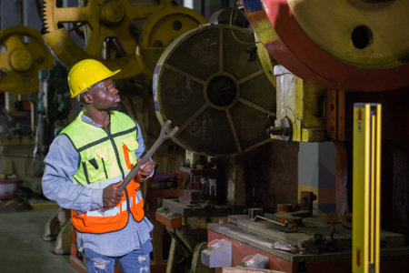 An individual in safety gear is in an industrial factory, holding a tool, working attentively.
