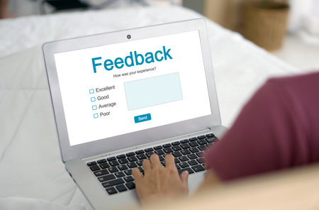 A focused woman is using her laptop, displaying the screen with the prominently visible word Feedback on it.の写真素材