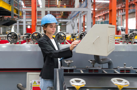A woman operates industrial equipment inside a busy factory setting, skillfully managing the...