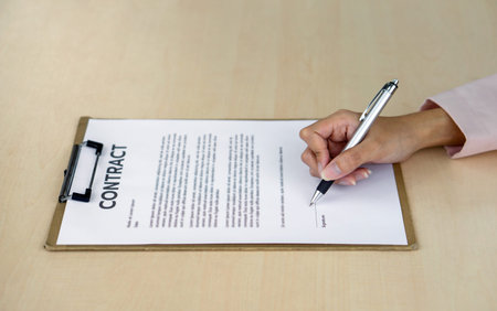 Closeup woman hand signing her name on a contract document on a board.