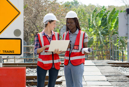 Two individual engaged in a discussion at a railway site, wearing safety equipment, including hard...