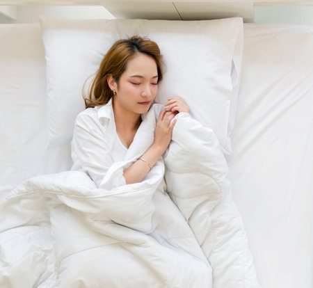 Young asian woman in white pajama, sleep and sweet dream lying on bed with soft pillows and a...