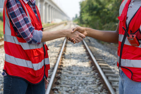 Two rail transportation engineer in reflective vest are shaking hands on some railroad tracks.の写真素材