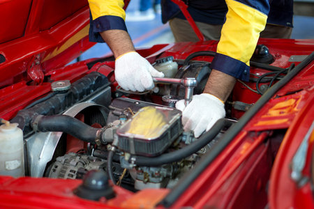 Closeup mechanic hand in work uniform, working on a car in an automotive shop or garage. He seem focused and engaged in diagnosing or repairing the vehicle's engine or other component.の写真素材