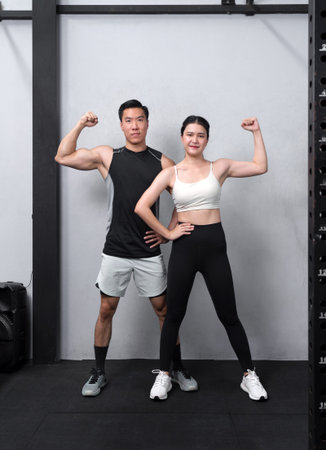 Empowered and strong, a fitness enthusiast couple flexes their biceps under the stark, vibrant...