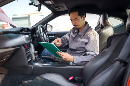 A mechanic in work uniform with a document clipboard, inspect a car coming for maintenance at a...