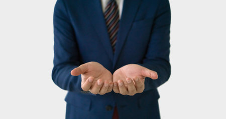 A businessman in smart blue suit and tie standing with his hand open and facing up, suggesting a gesture of offering, explaining, or questioning. Portrait on white background, studio shot.の写真素材