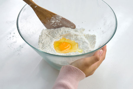 Closeup hand holding glass bowl with an egg and flour, preparing to bake.の写真素材