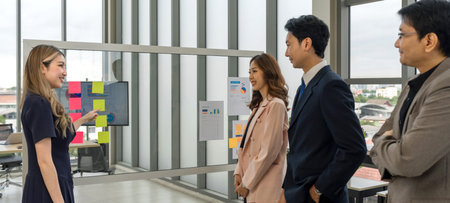 A professional man and woman stand together, engaged in a brainstorming session, using document and...