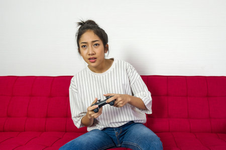 Young asian woman playing console game relax in living room, enjoy leisure weekend at home. Stress free concept.の写真素材