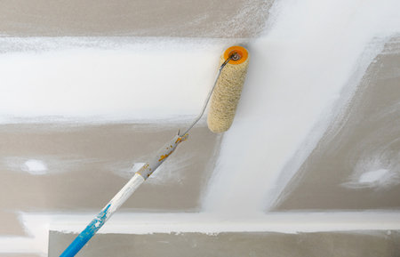 A paint roller is being used to apply a fresh coat of white paint on the ceiling of a newly renovated room. The wall have a smooth finish, indicating recent update.の写真素材