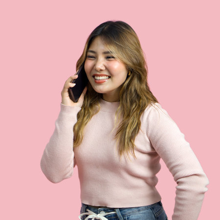 Young asian woman in casual clothing is talking on her smartphone. Portrait on a simple pink background with studio light. Isolatedの写真素材