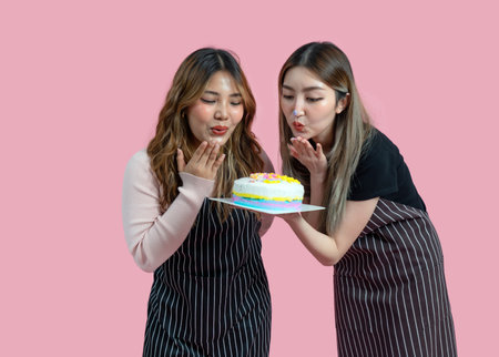 Young asian couple with apron in celebratory or festive mood holding colorful cake. Portrait on pink background with studio light, Isolated.の写真素材
