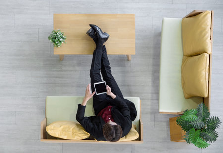 Young businessman in suit sit relax on sofa, rest his feet on the table while use tablet computer searching for interesting investment information. Top Viewの写真素材