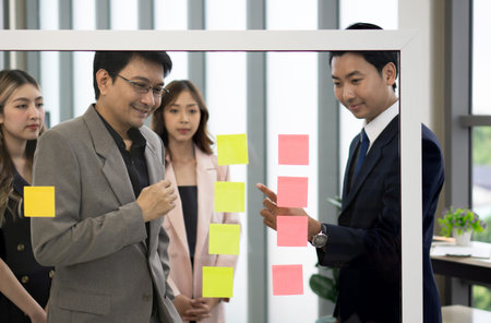 A professional man and woman stand together, engaged in a brainstorming session, using document and...