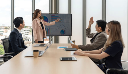 Asian businessman in suit raise his hand to ask a question to presenter standing in front of a large...