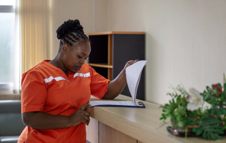 A female healthcare worker in an orange uniform stand at a counter, focused on reading a document.の写真素材