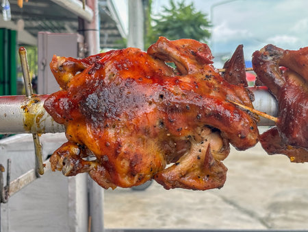 Juicy whole chicken are roasting on a rotisserie over charcoal at a street vendor stall. Close upの写真素材