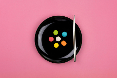 Top view of mini colorful Macarons on the black plate with a pair of chopsticks, pink table.の写真素材