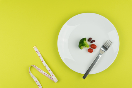 Diet concept : small amount of food on the white plate with a measuring tape.の写真素材