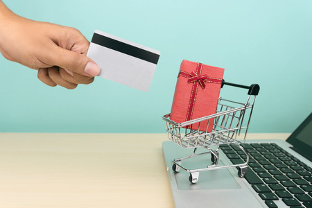 hand holding credit card, a red gift box in a shopping cart on a laptop, e-commerce or online shopping conceptの写真素材