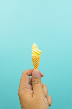 hand holding a mini vanilla soft ice cream in wafer cone on blue backgroundの写真素材