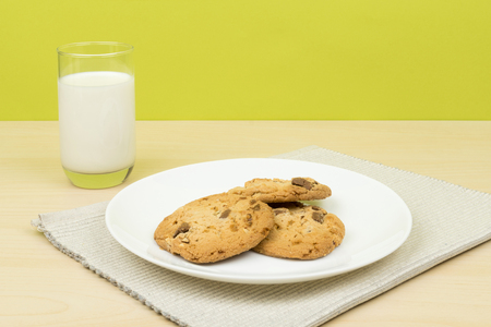 a glass of milk, three pieces of chocolate chip cookies in a white round dish on the wooden table. green backgroundの写真素材