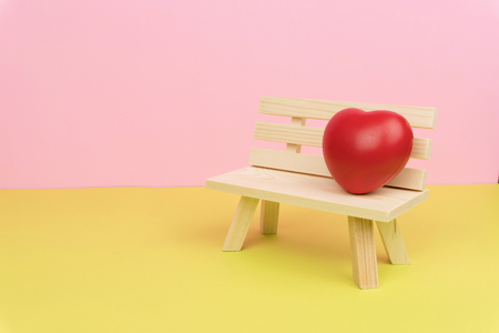 lonely heart concept, a red love heart symbol on the wooden bench with pink and green backgroundの写真素材