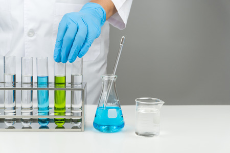 laboratory scene, the scientist putting the test tube into rack, flask and beaker on the tableの写真素材