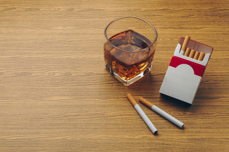 a glass of bourbon whiskey, two cigarettes with a cigarette pack on the wooden tableの写真素材