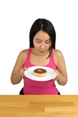 beautiful plus size Asian woman sitting at the wooden table and holding a plate with doughnut on white backgroundの写真素材